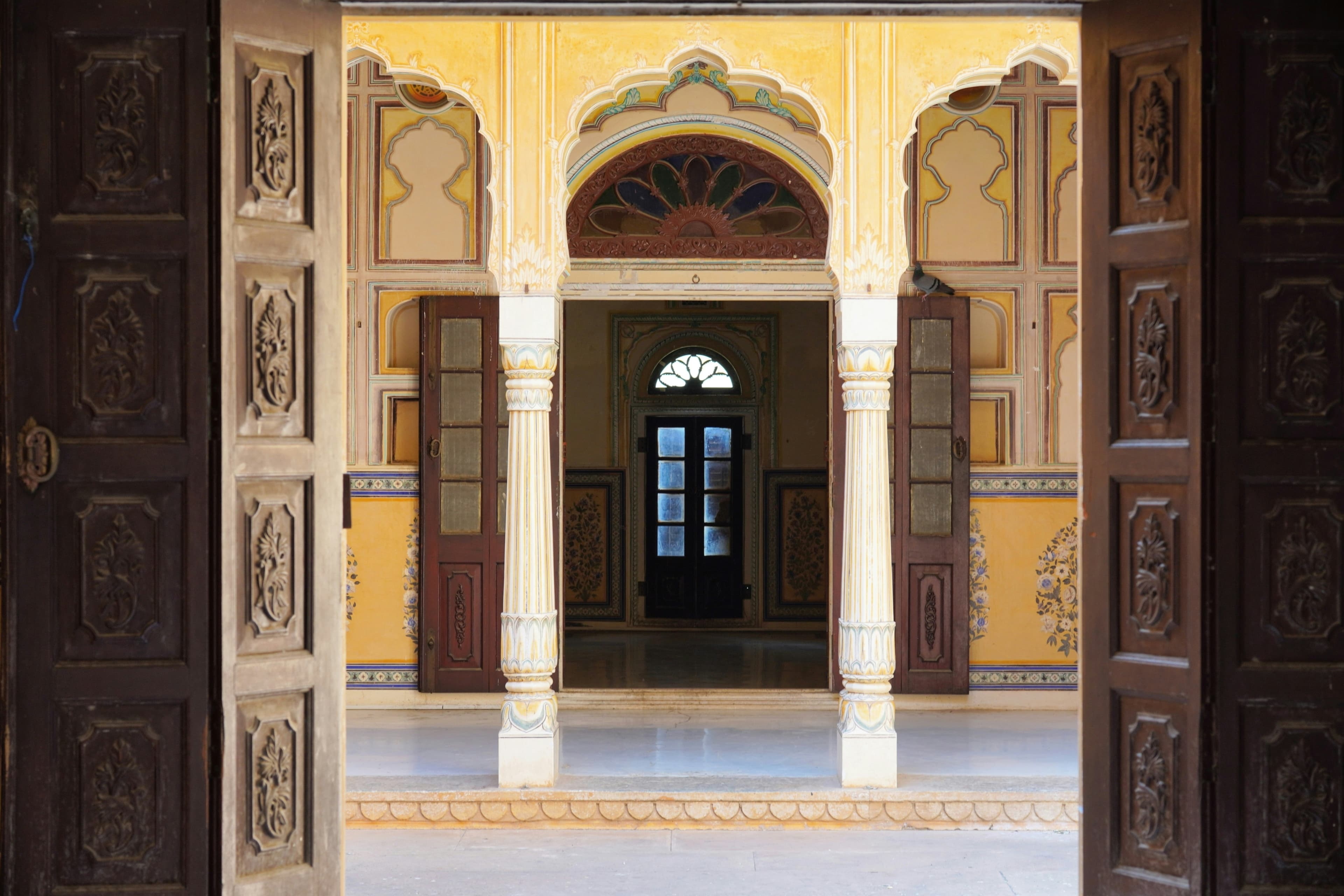 Open carved wooden doors framing a yellow painted courtyard with slender white columns