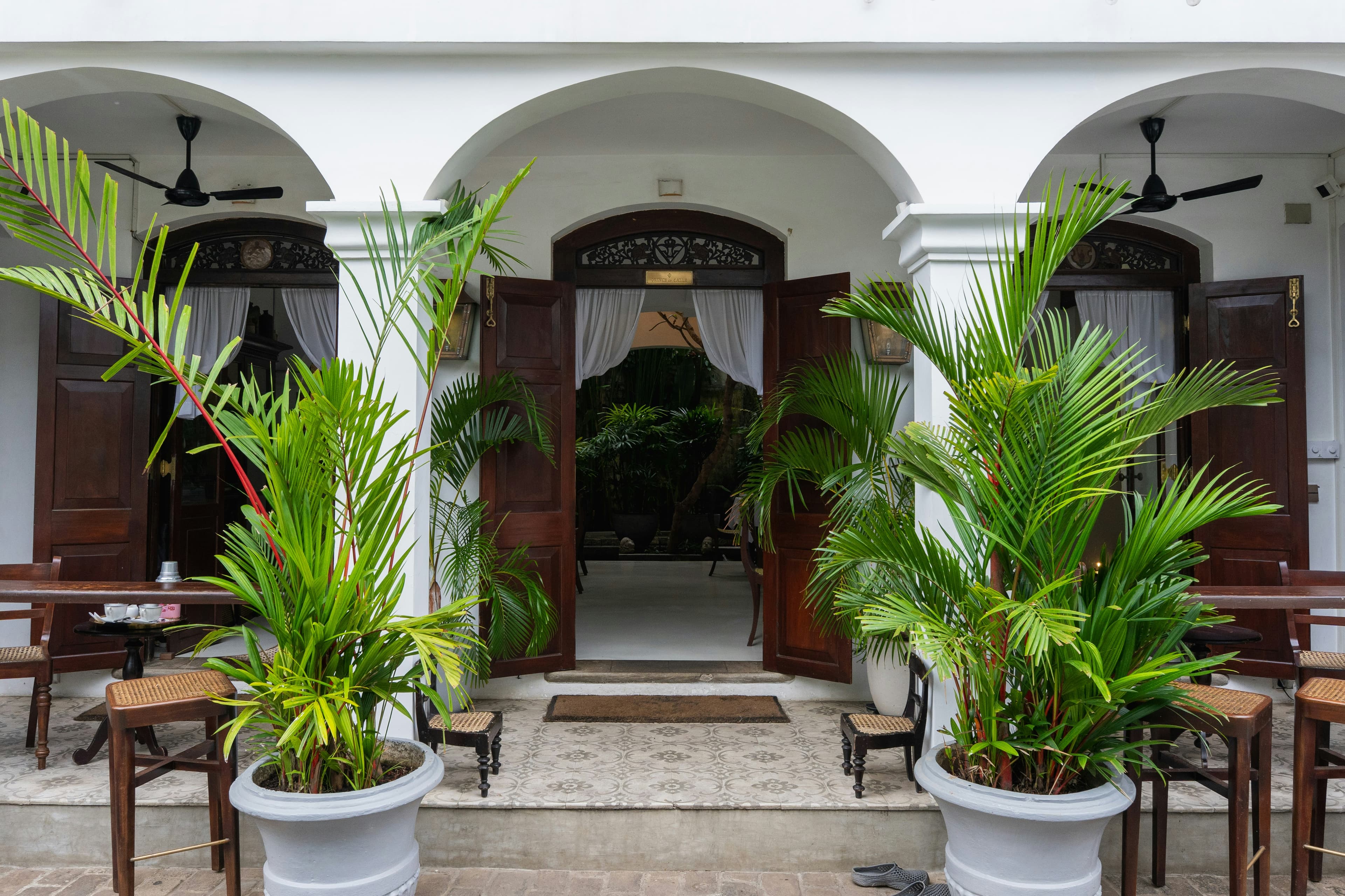 White colonial arches with open dark wood doors, framed by tall potted palms